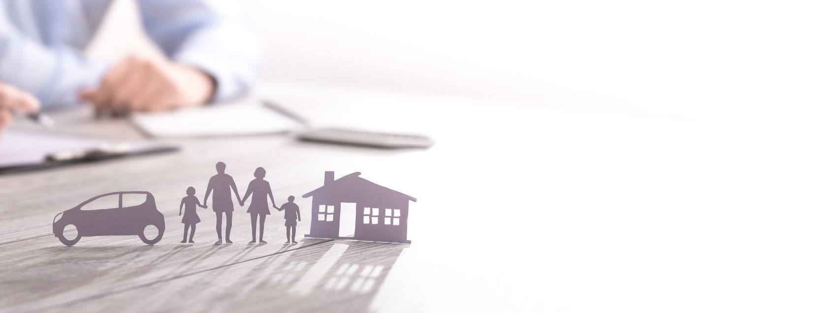 paper cut out of family and a house with a person signing a contract in the background