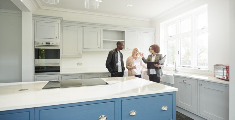 a saleswoman or estate agent shows a couple around a home with new kitchen