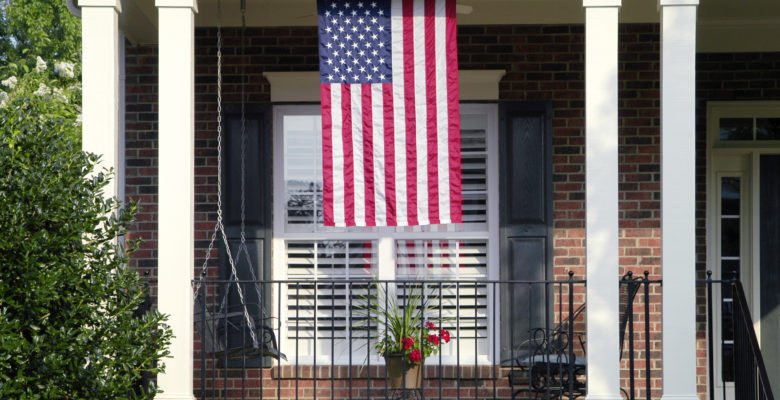 Detail of a traditional brick home with an American Flag hanging from the front of the house.