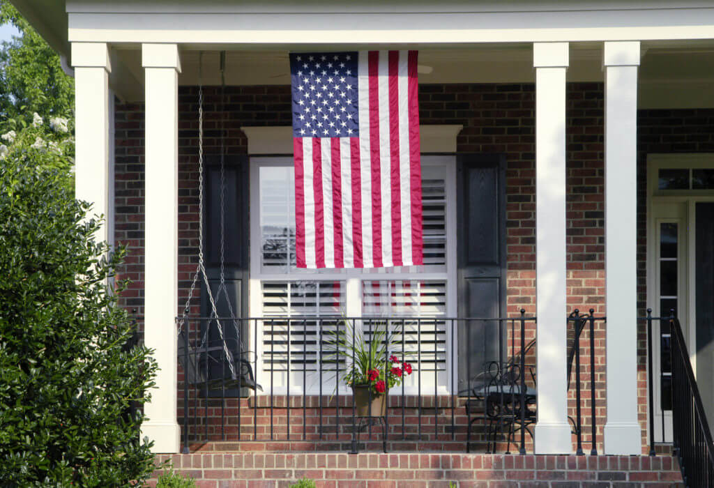 Detail of a traditional brick home with an American Flag hanging from the front of the house.